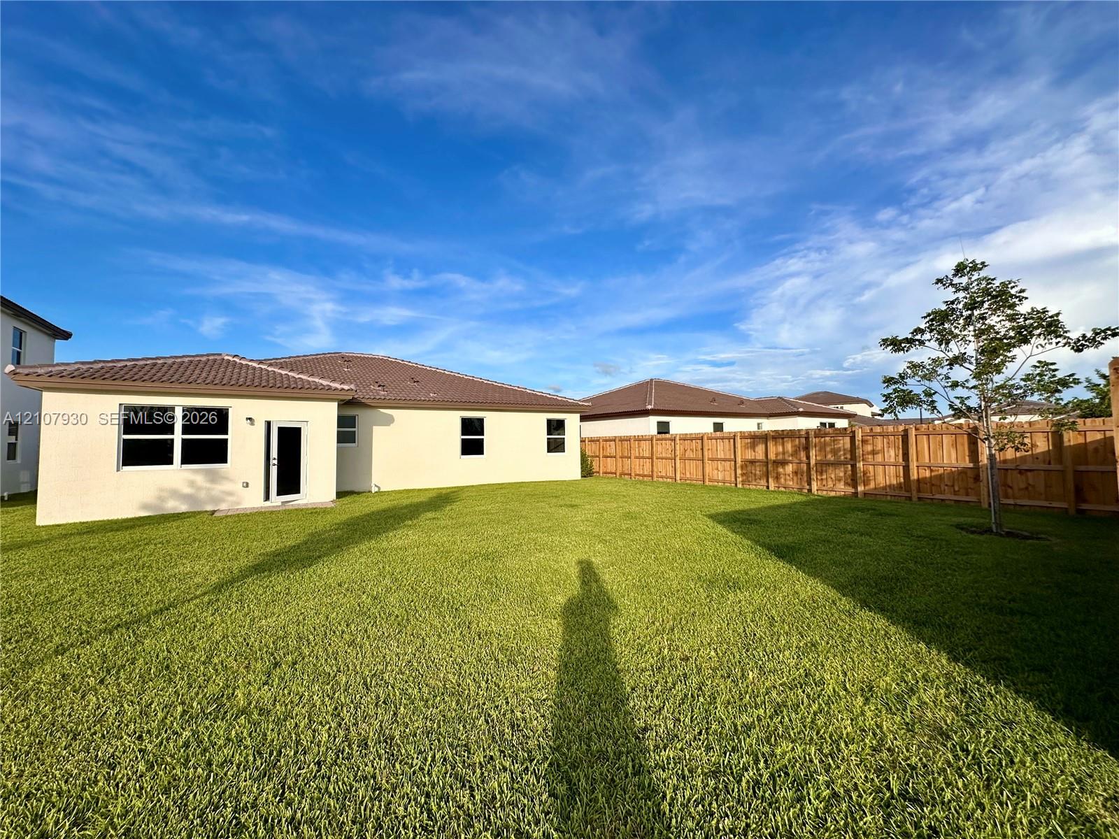 Spacious backyard featuring a grass lawn, perimeter wood fencing, and a stucco exterior with a tiled roof Spacious backyard featuring a grass lawn, perimeter wood fencing, and a stucco exterior with a tiled roof