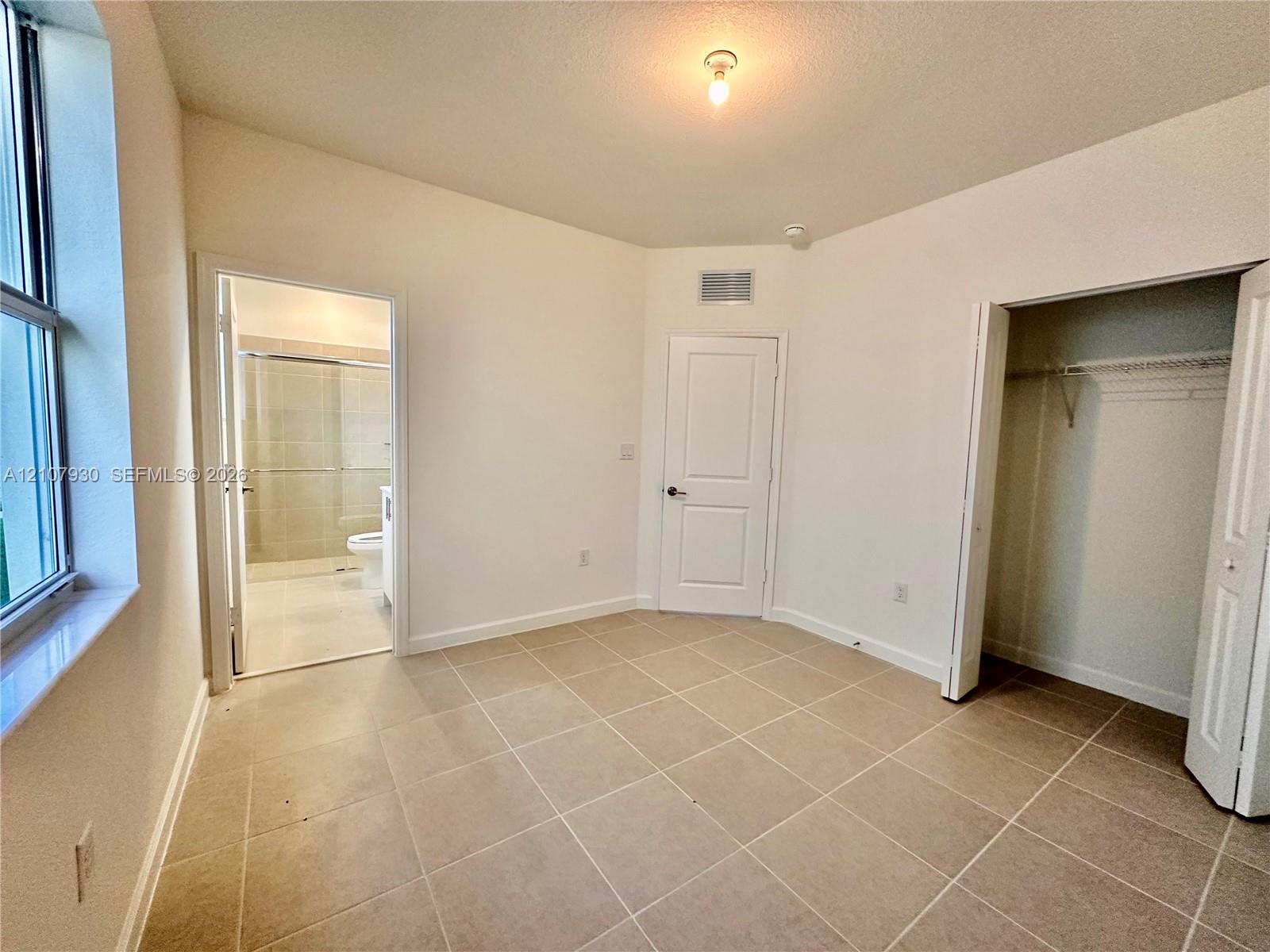 Room featuring tile flooring, neutral wall color, multi-panel interior door, walk-in closet with built-in shelving, and flush-mount ceiling light