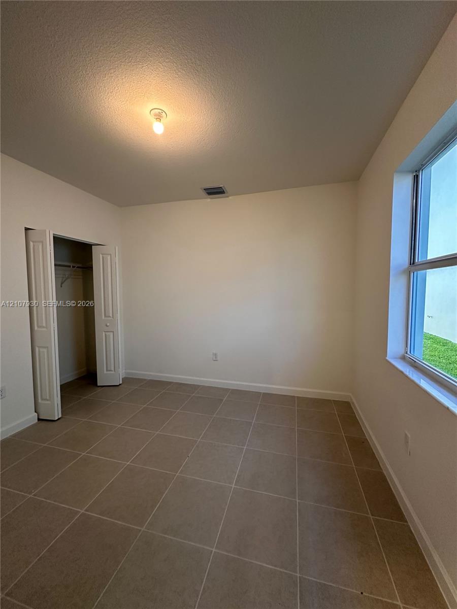 Room featuring neutral-toned tile flooring, light-colored walls, a double-door closet with internal shelving, and a window with a stone sill
