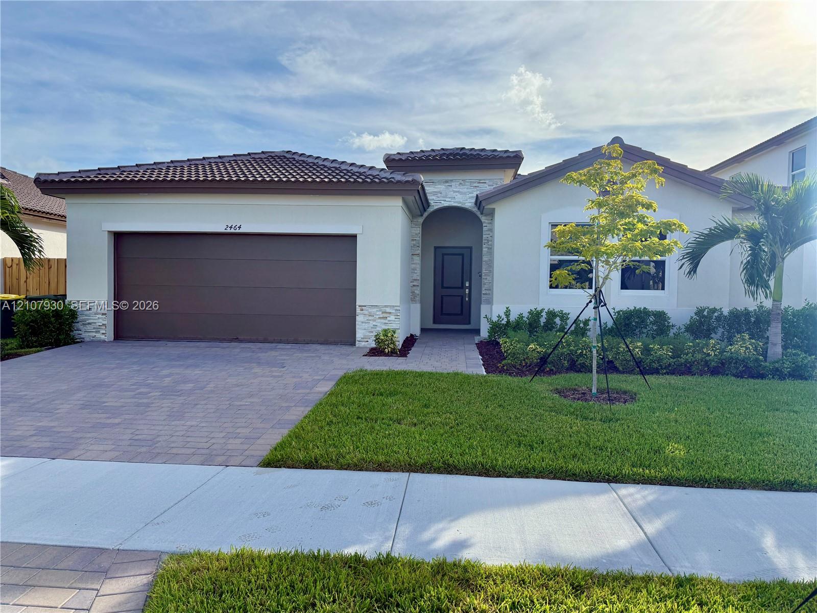 Single-story residence featuring a tile roof, exterior stone accents, a multi-car garage, and a paved driveway Single-story residence featuring a tile roof, exterior stone accents, a multi-car garage, and a paved driveway