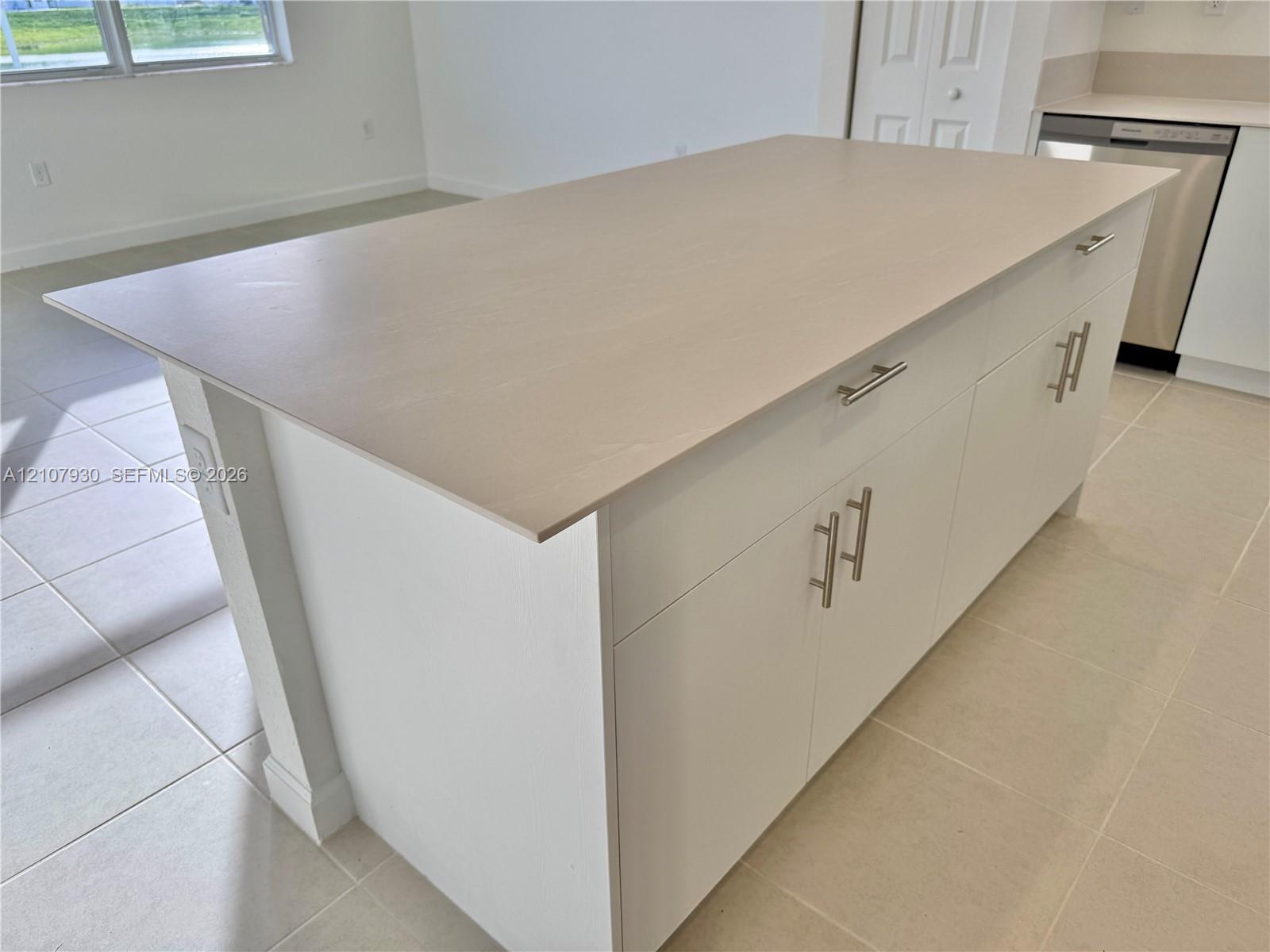 Kitchen island featuring a flat-surface countertop, white cabinetry, satin-finish hardware, and tile flooring