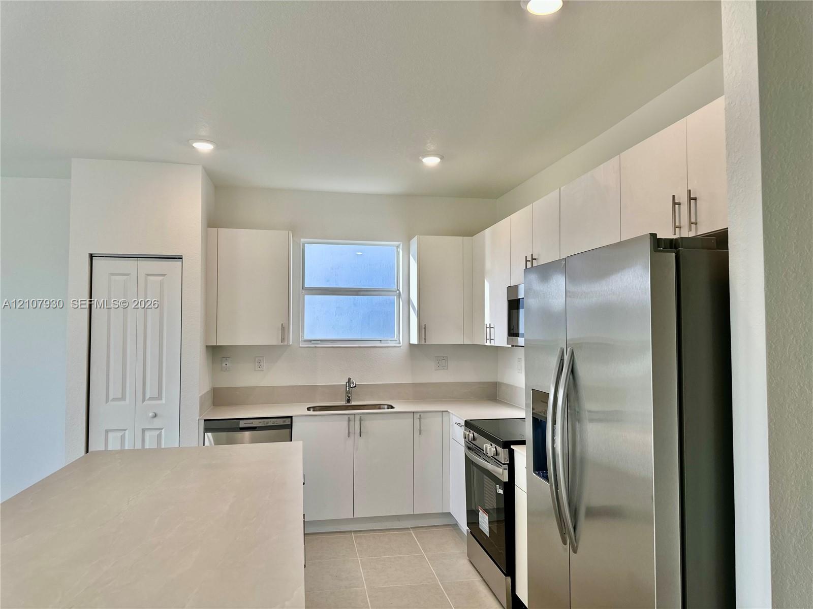 Kitchen featuring white flat-panel cabinetry, stainless steel appliances, a central island with a solid surface countertop, and tile flooring