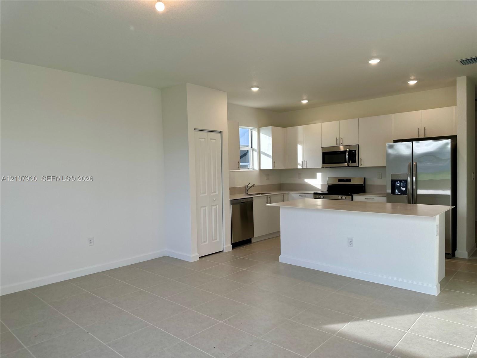 Kitchen featuring white cabinetry, an island with countertop seating, stainless steel appliances, and large-format tile flooring