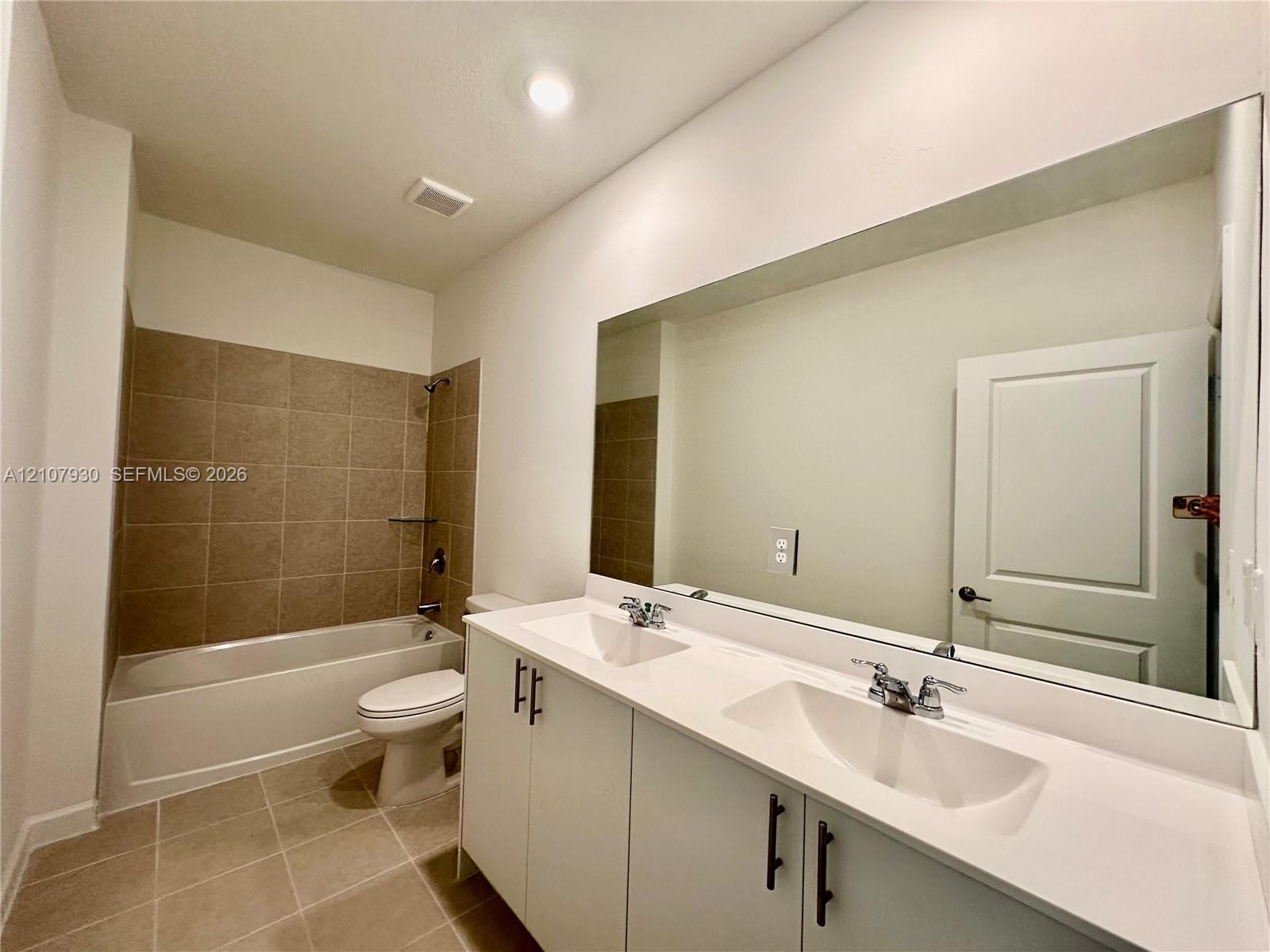 Double vanity featuring white cabinetry, a solid surface countertop, rectangular under-mount sinks, and a full-width mirror, accompanied by a bathtub with tiled surround