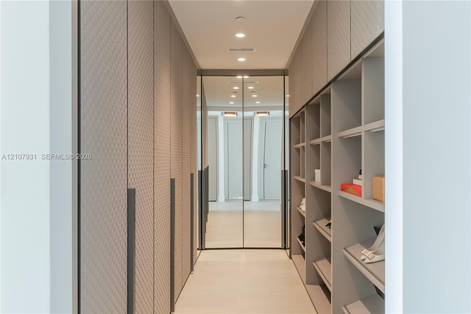 Custom storage solution featuring floor-to-ceiling cabinetry with textured diamond-patterned doors, integrated full-height mirrors, extensive open shelving, and recessed ceiling lighting