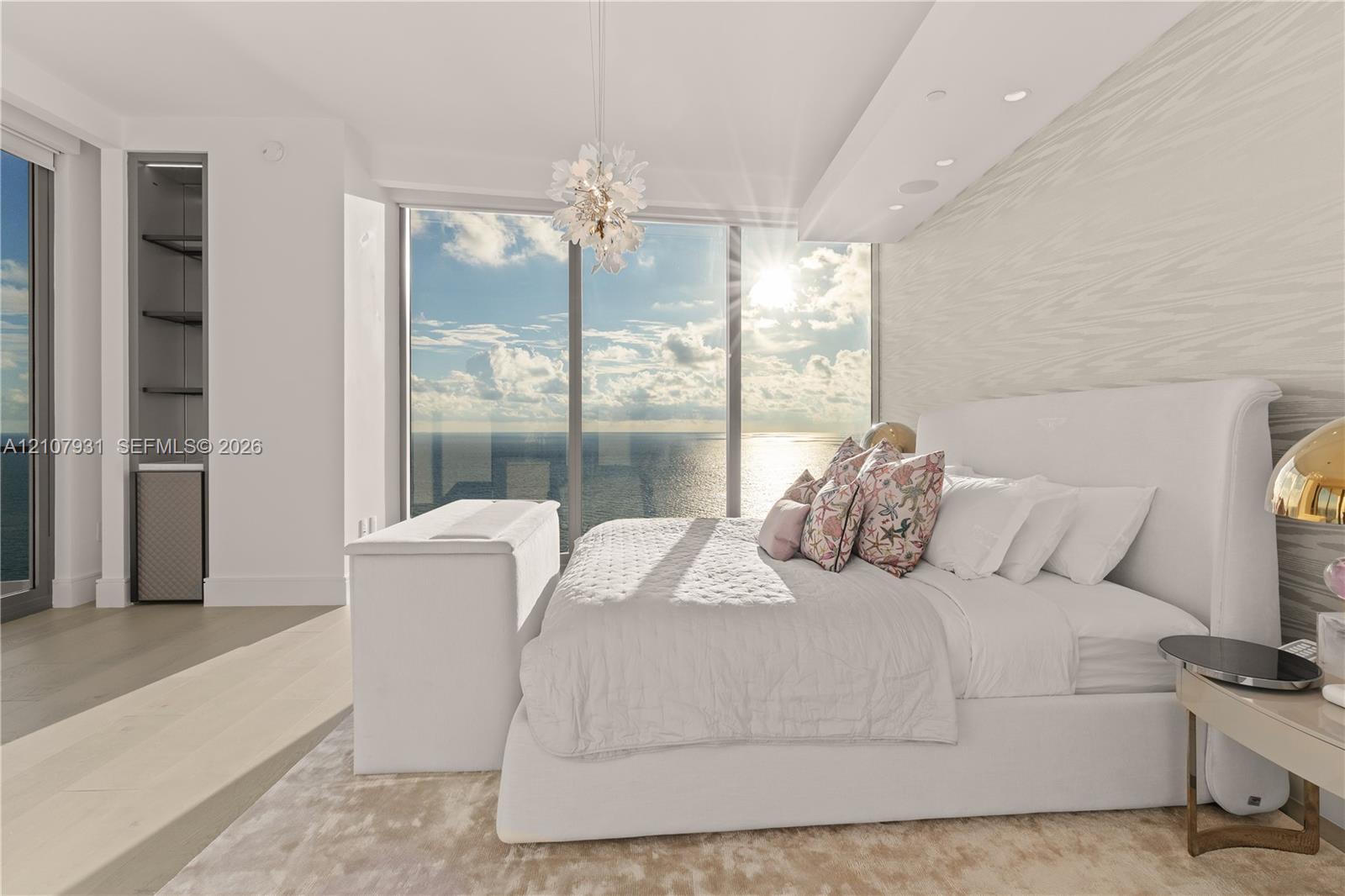 Floor-to-ceiling windows, textured accent wall, integrated recessed lighting, light wood-finish flooring, and a contemporary crystal chandelier