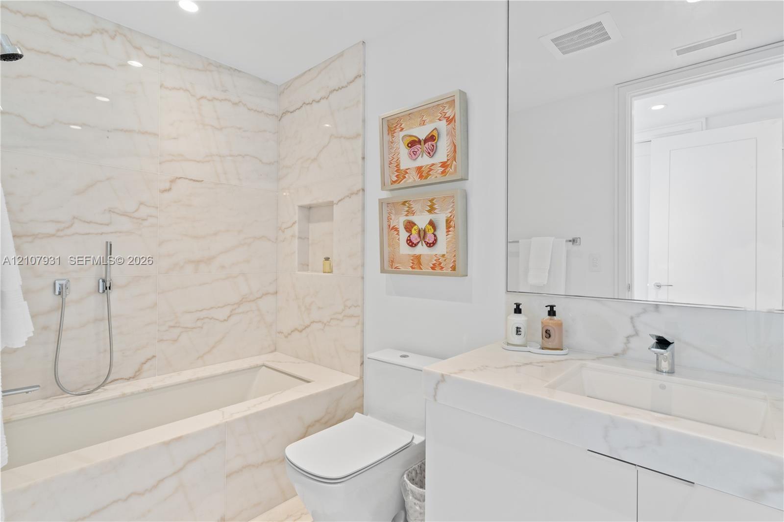 Full-height slab-stone wall surround, integrated recessed shower niche, modern white vanity with matching stone countertop, rectangular undermount sink, and wall-to-wall vanity mirror