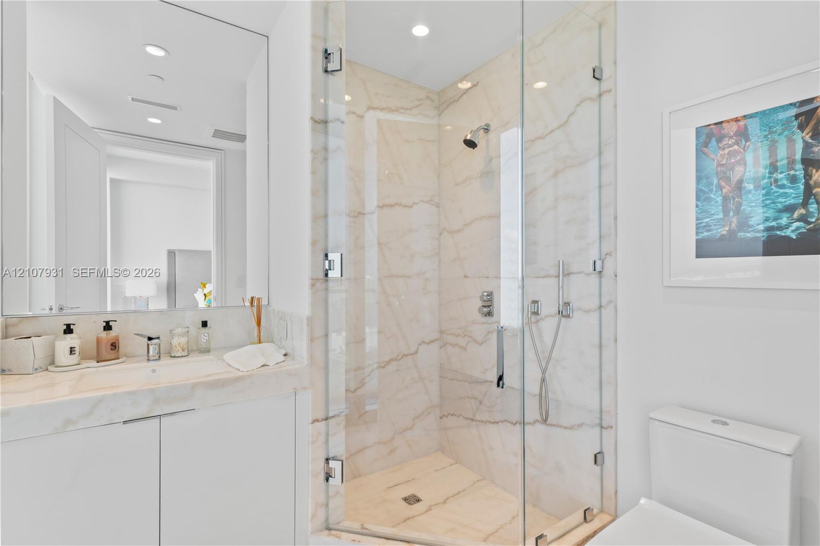 Bathroom featuring a vanity with integrated sink and stone countertop, frameless glass-enclosed shower with stone-surround, wall-to-wall mirror, and recessed lighting