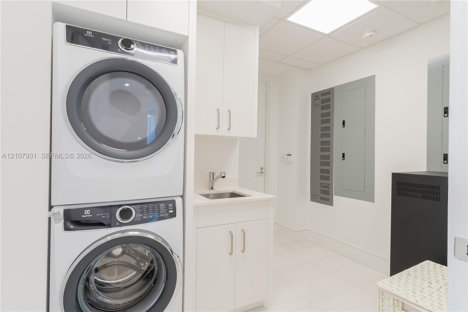 Laundry room featuring a stacked appliance set, white cabinetry, a built-in sink with a chrome faucet, and tile flooring