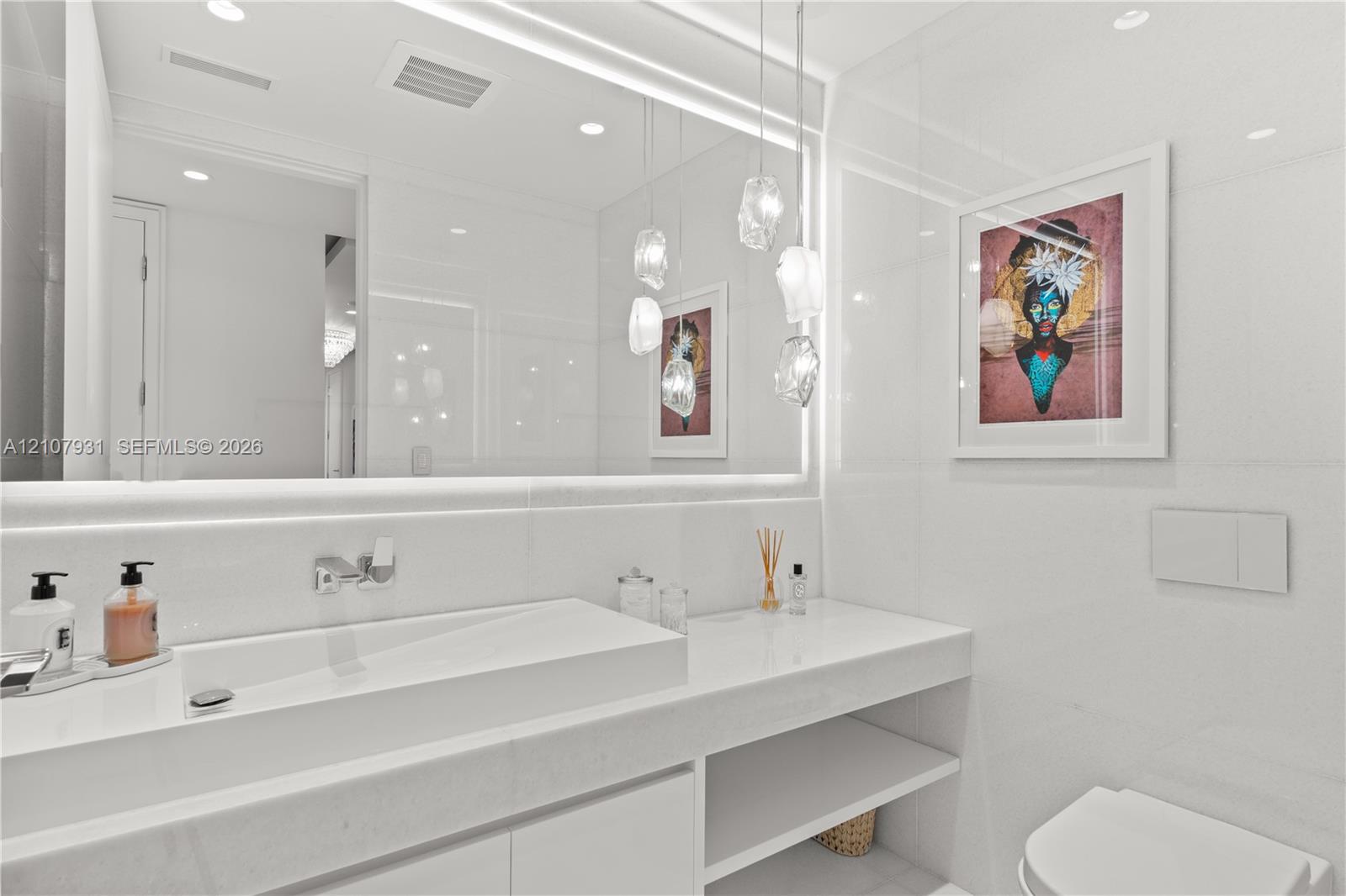 Floating vanity with an integrated basin, expansive wall-to-wall mirror, tiered glass pendant lighting, and recessed ceiling illumination