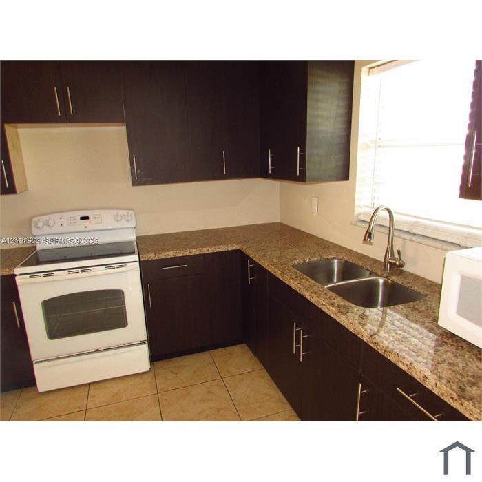 Kitchen featuring dark-toned cabinetry, stone-finish countertops, stainless steel dual-basin undermount sink with a gooseneck faucet, white electric range, and tile flooring