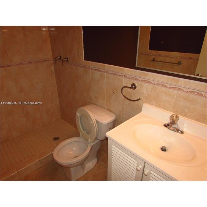 Bathroom featuring full-height wall tiling with decorative accent trim, a stall shower, a vanity with a molded countertop and integrated basin, and louvered-style cabinet doors