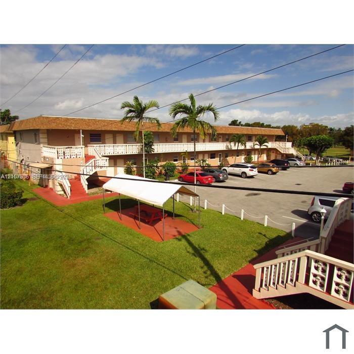Multi-story building with a shingle-style roof, exterior staircases, designated paved parking area, and landscaped grounds featuring palm trees
