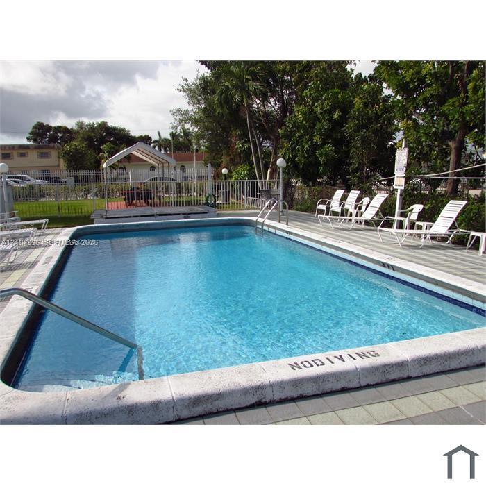 Rectangular in-ground swimming pool featuring a concrete coping surround, metal pool ladder, and expansive light-toned paver deck