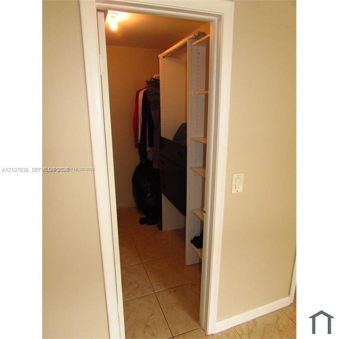 Walk-in closet featuring floor-to-ceiling shelving, built-in storage drawers, a hanging rod, and ceramic tile flooring