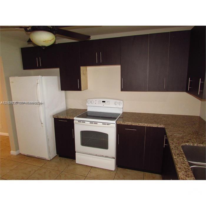 Kitchen featuring dark wood-finish cabinetry, stone-surface countertops, dual-basin stainless steel sink, and white appliances including a freestanding range and refrigerator