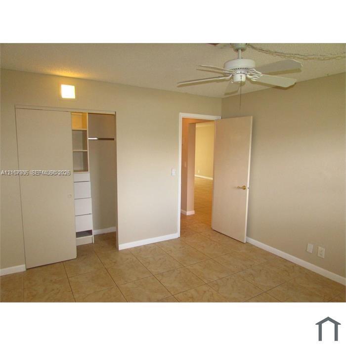Ceramic tile flooring, white ceiling fan with integrated lighting, and built-in closet cabinetry with shelving and drawers