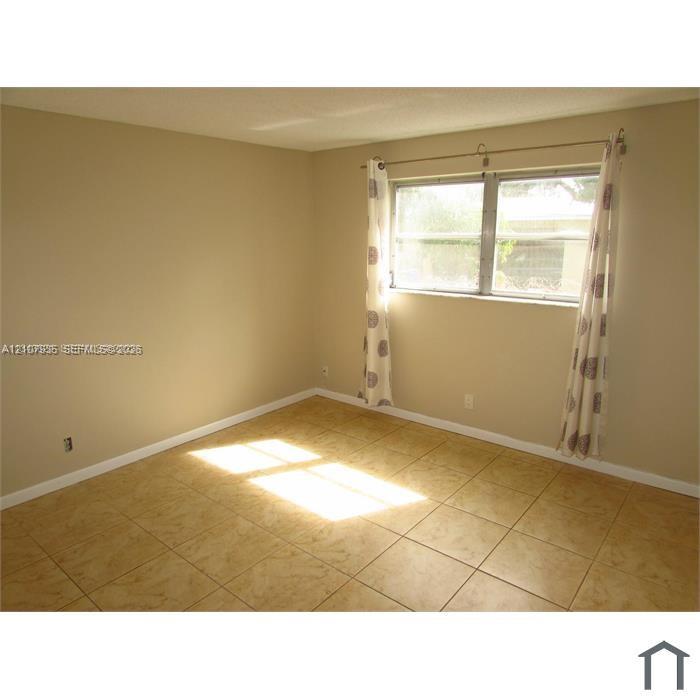Neutral-toned interior room featuring large-format ceramic tile flooring, a horizontal sliding window, and a metal curtain rod fixture