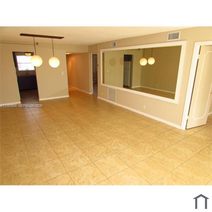 Neutral-toned interior space featuring light-colored square tile flooring, a large wall-mounted mirror with white trim, and a modern two-globe pendant light fixture