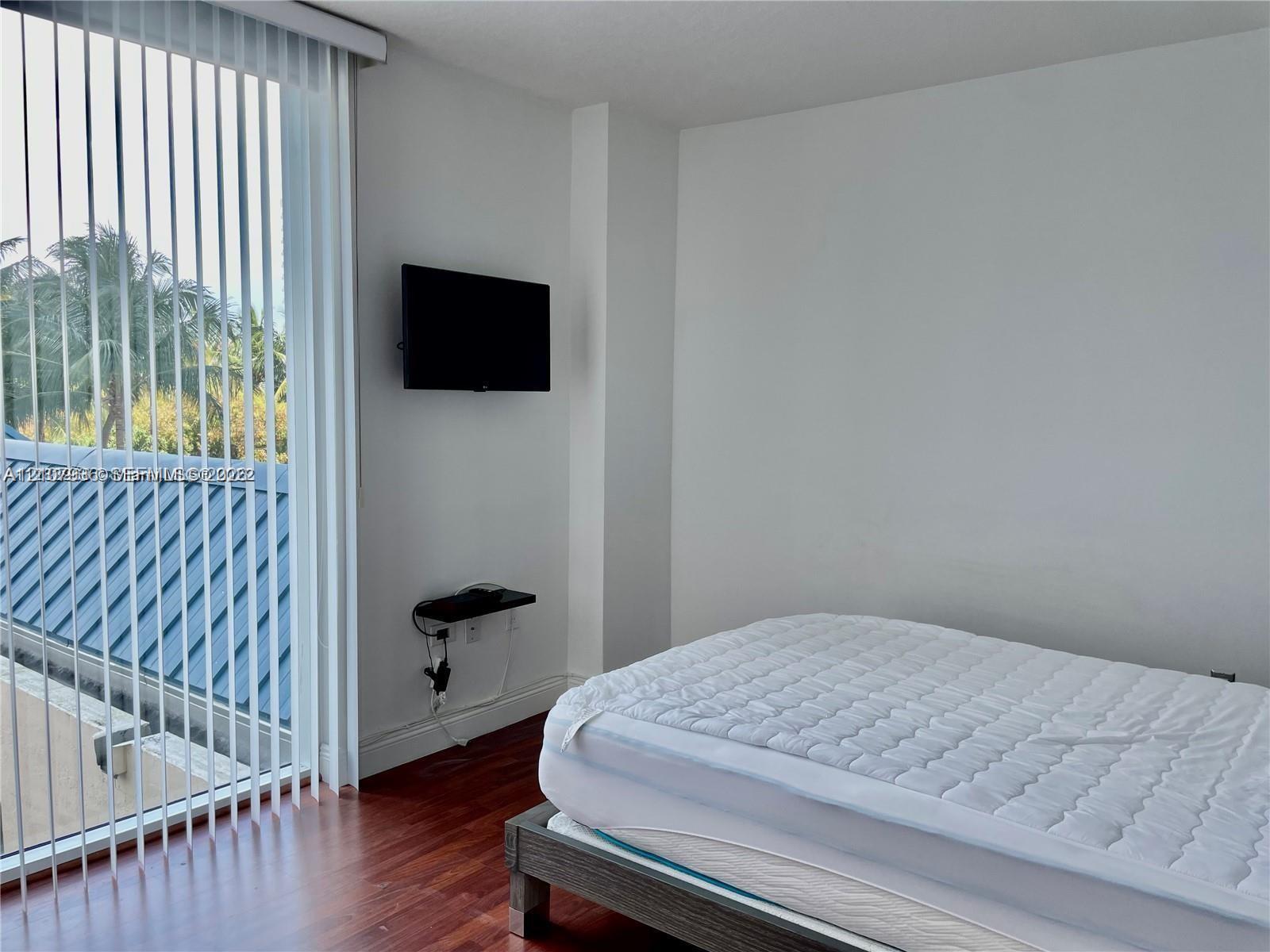 Floor-to-ceiling vertical blinds, wood-finish flooring, and a wall-mounted floating media shelf