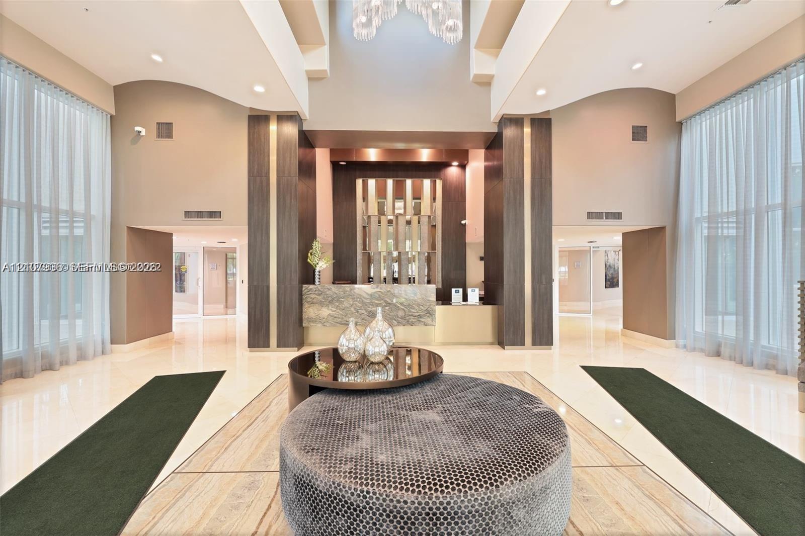 Double-height ceiling, floor-to-ceiling windows, polished stone flooring, custom architectural columns, and a stone-clad reception desk