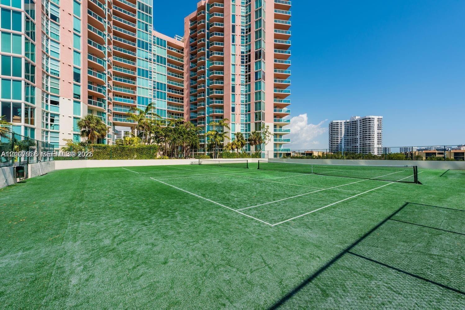 Outdoor tennis court featuring artificial turf surfacing, perimeter fencing, and net equipment
