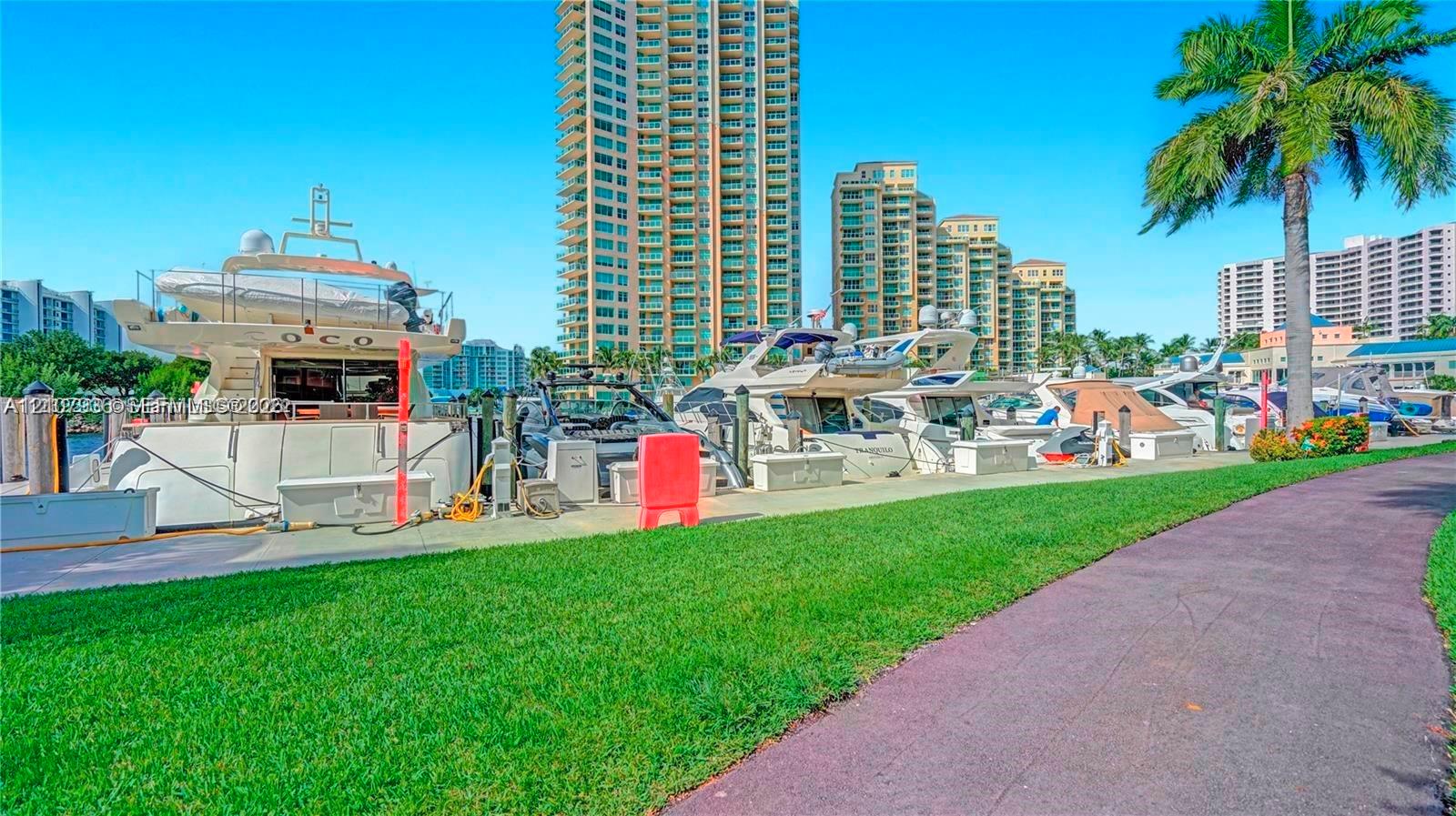 Waterfront promenade featuring a paved walkway, manicured lawn, and deep-water marina access