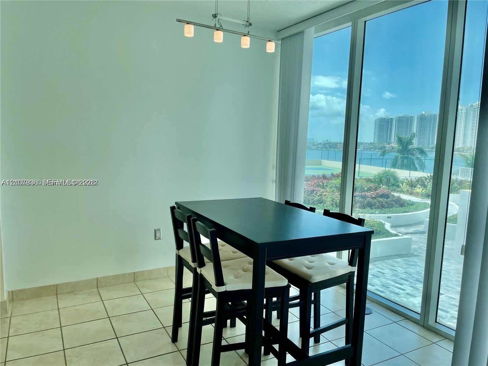 Floor-to-ceiling windows, tile flooring, four-light brushed metal track lighting, and exterior water backdrop