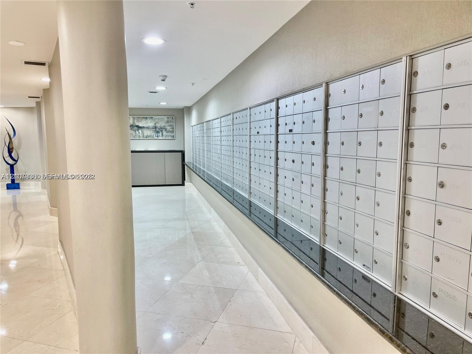 Common area mail center featuring a wall of individual metal mailboxes, a dark stone ledge, recessed ceiling lighting, and polished stone tile flooring
