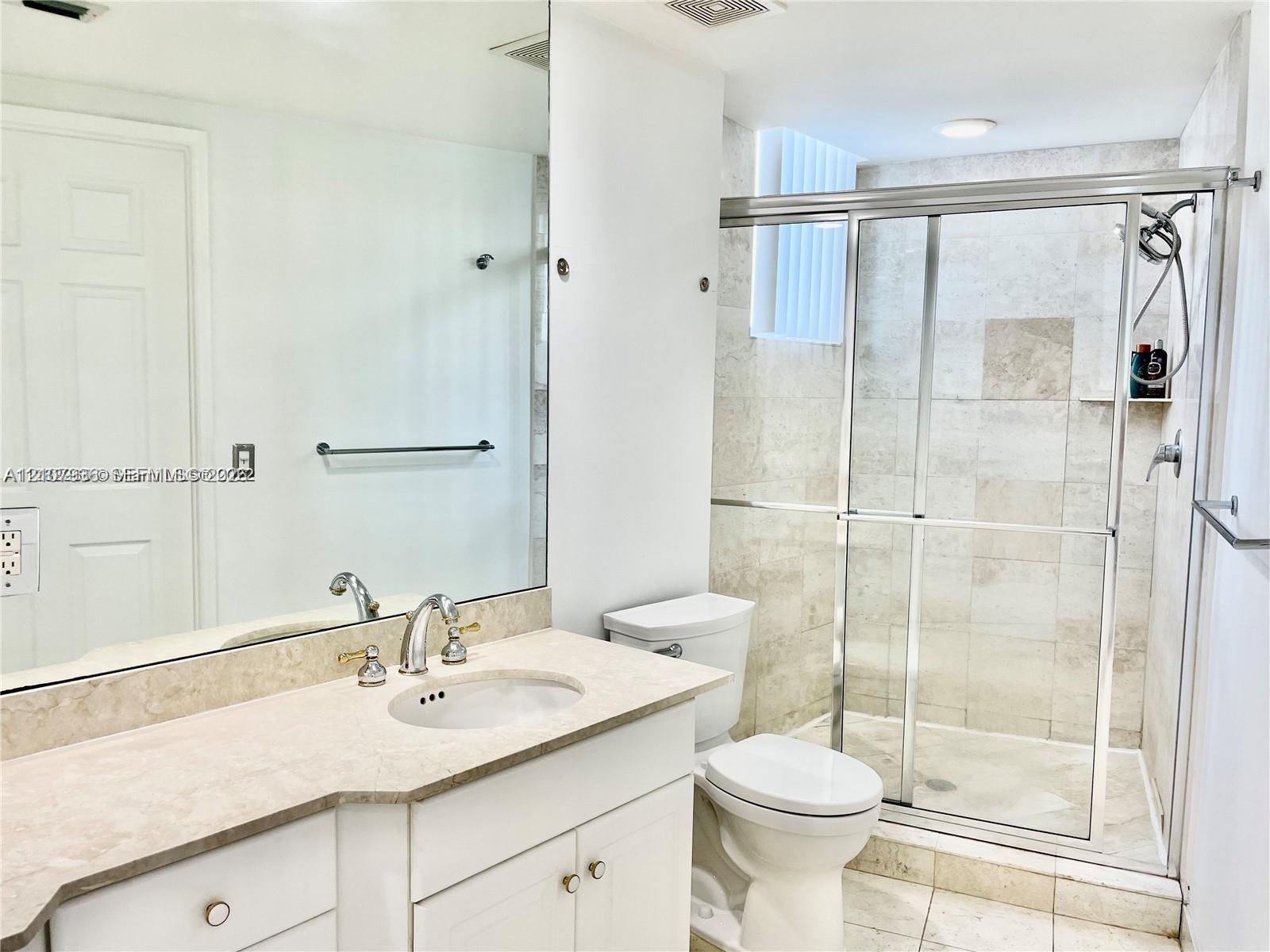 Bathroom featuring a vanity with a stone countertop, an integrated sink, an expansive wall-mounted mirror, a glass-enclosed shower with stone tile surround, and tile flooring