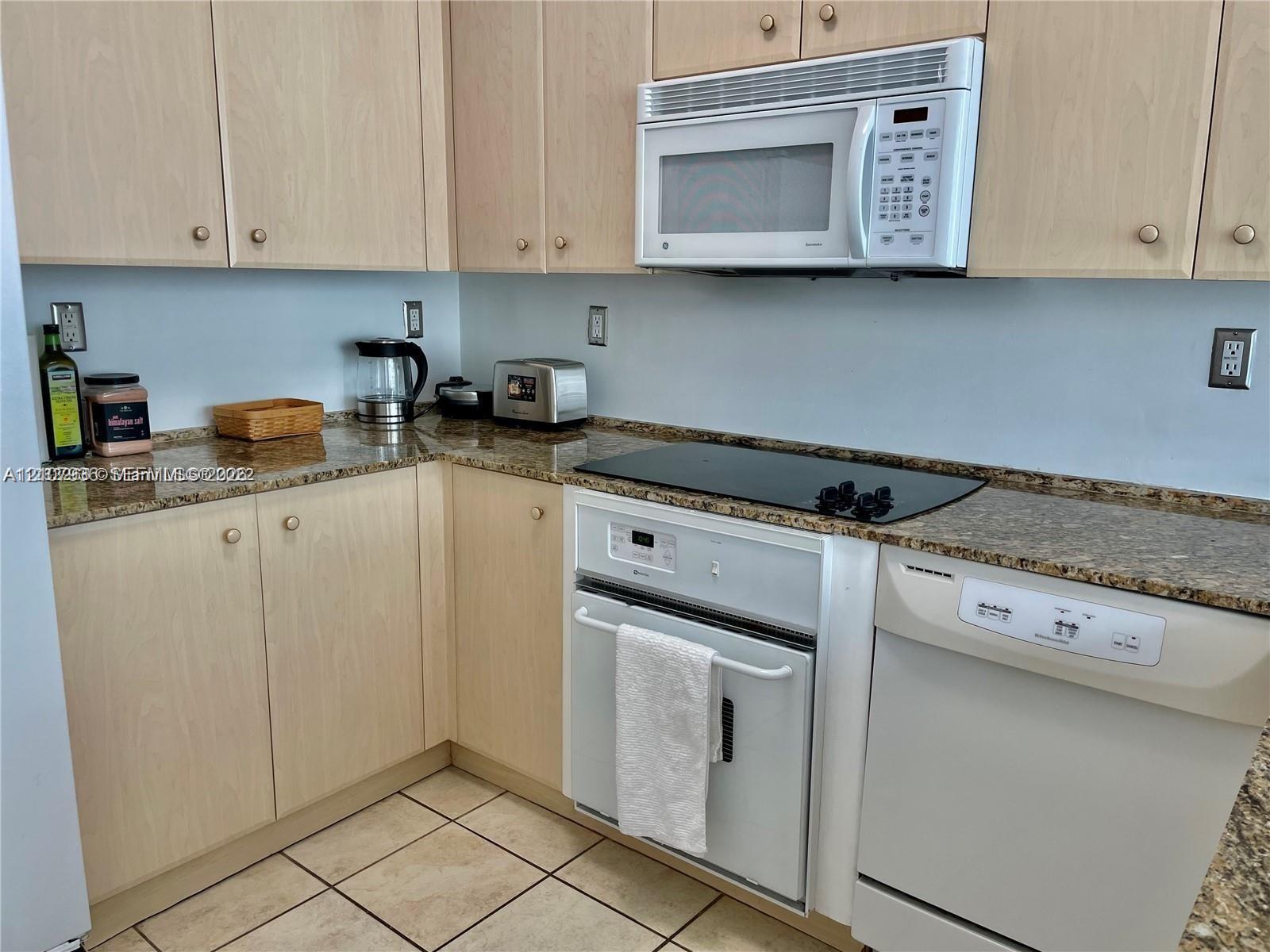 Kitchen featuring light-finish cabinetry, stone-texture countertops, ceramic tile flooring, and built-in appliances including a microwave, oven, and dishwasher