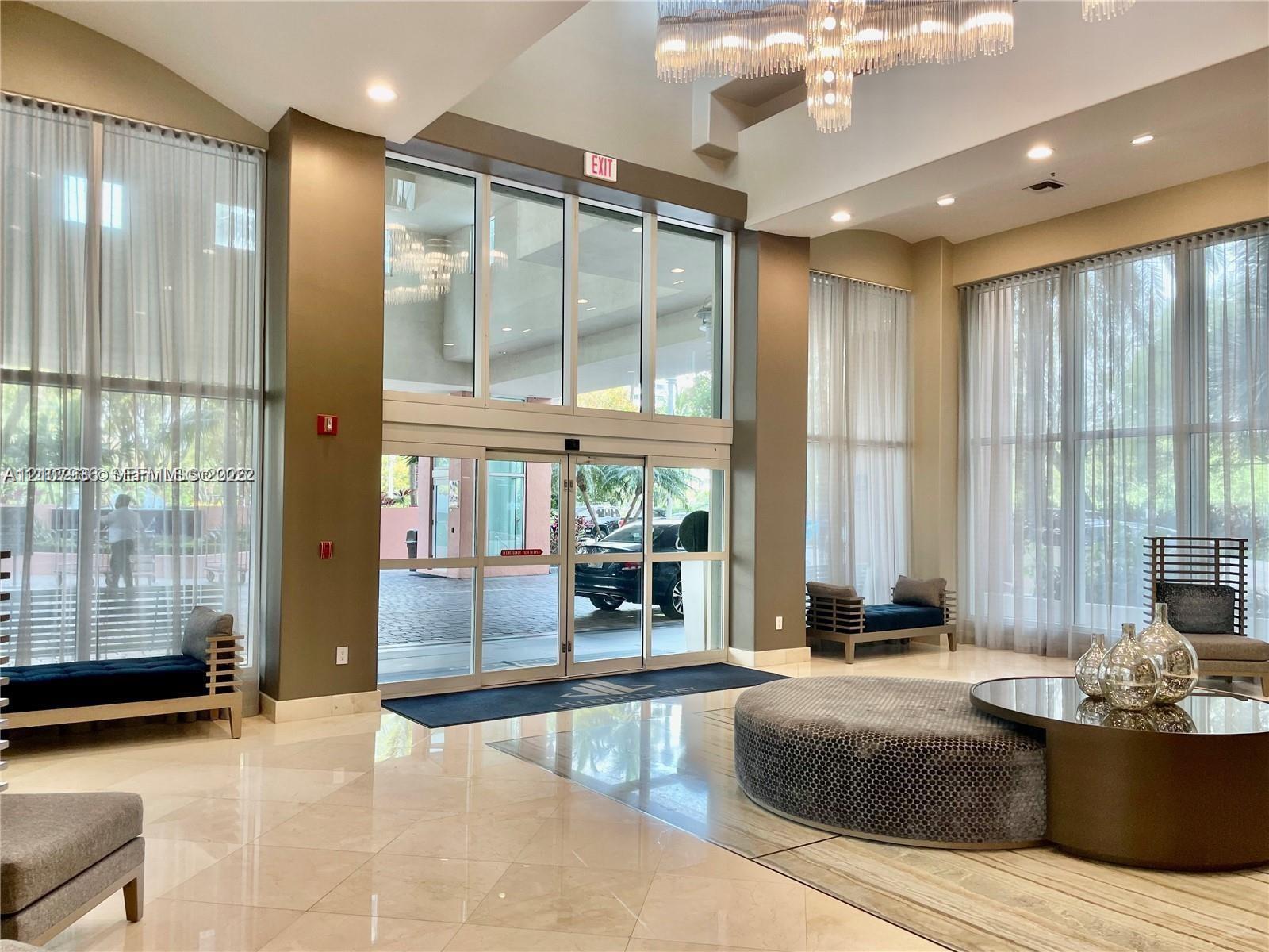 Double-height glass entrance featuring soaring floor-to-ceiling windows, polished stone flooring, recessed lighting, and a multi-tiered crystal chandelier