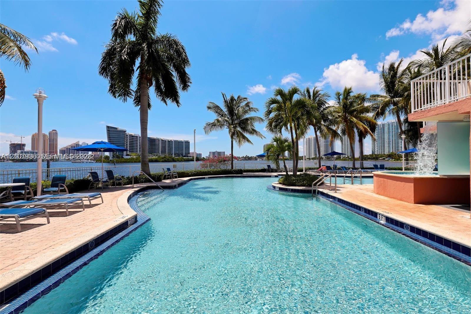 Waterfront swimming pool with an integrated spa, featuring paved decking and mature palm trees