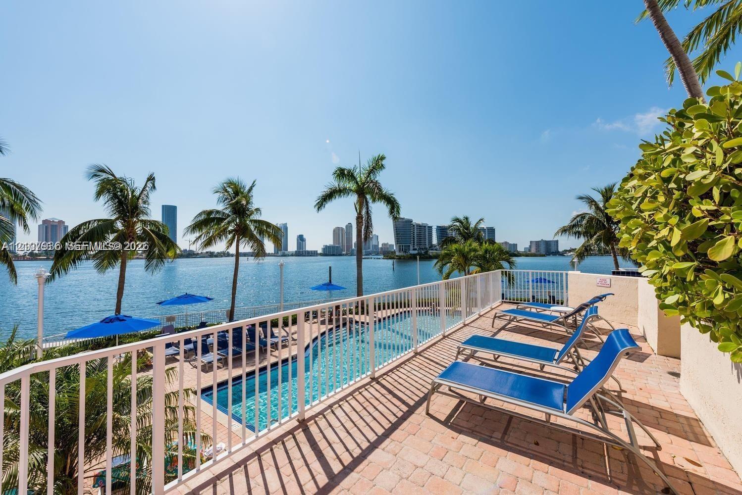 Waterfront terrace featuring a paver deck, white metal railing, and an in-ground swimming pool overlooking the bay