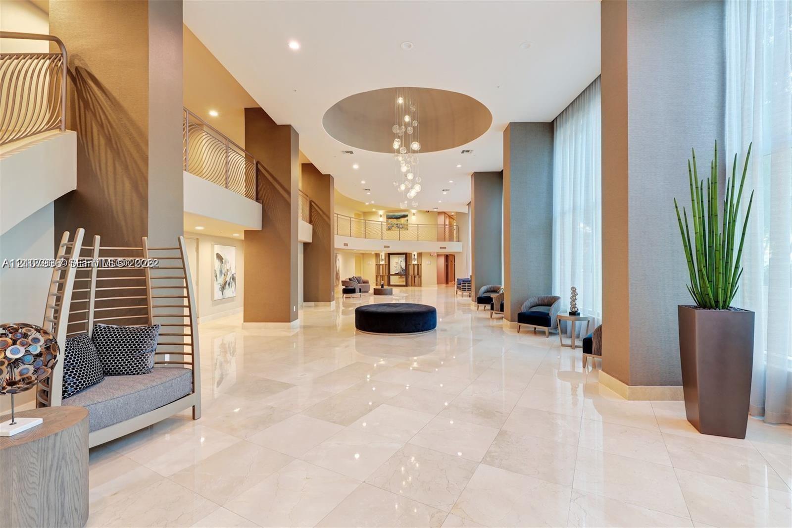 Grand lobby featuring high ceilings, polished stone flooring, a multi-tiered circular ceiling medallion with recessed lighting, suspended light fixtures, and a structural mezzanine level with metal railings