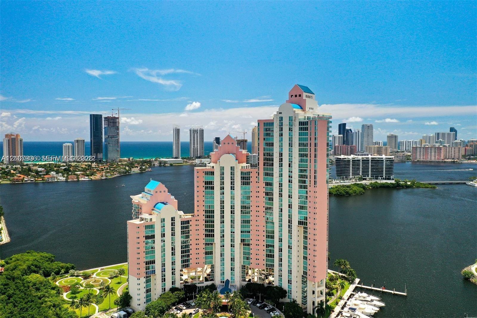 High-rise building with a tiered architectural design, multi-story glass-paned windows, waterfront location, manicured landscaped grounds, and integrated boat slips