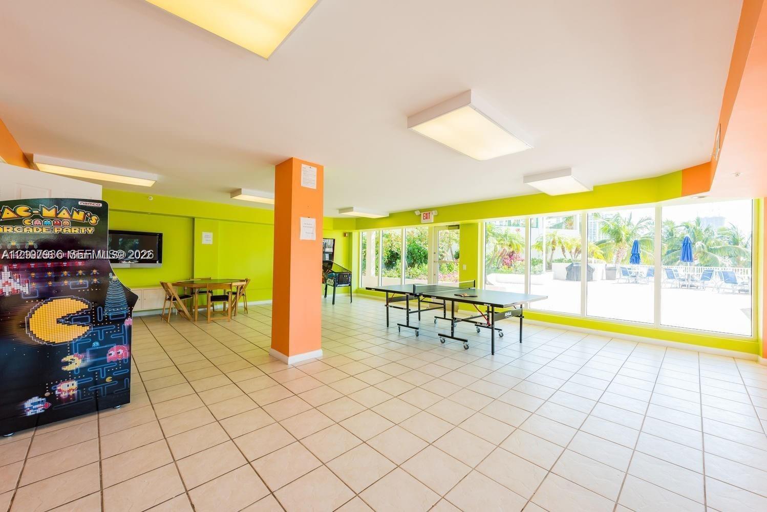 Open-plan recreation area featuring ceramic tile flooring, recessed panel lighting, and floor-to-ceiling windows providing natural light