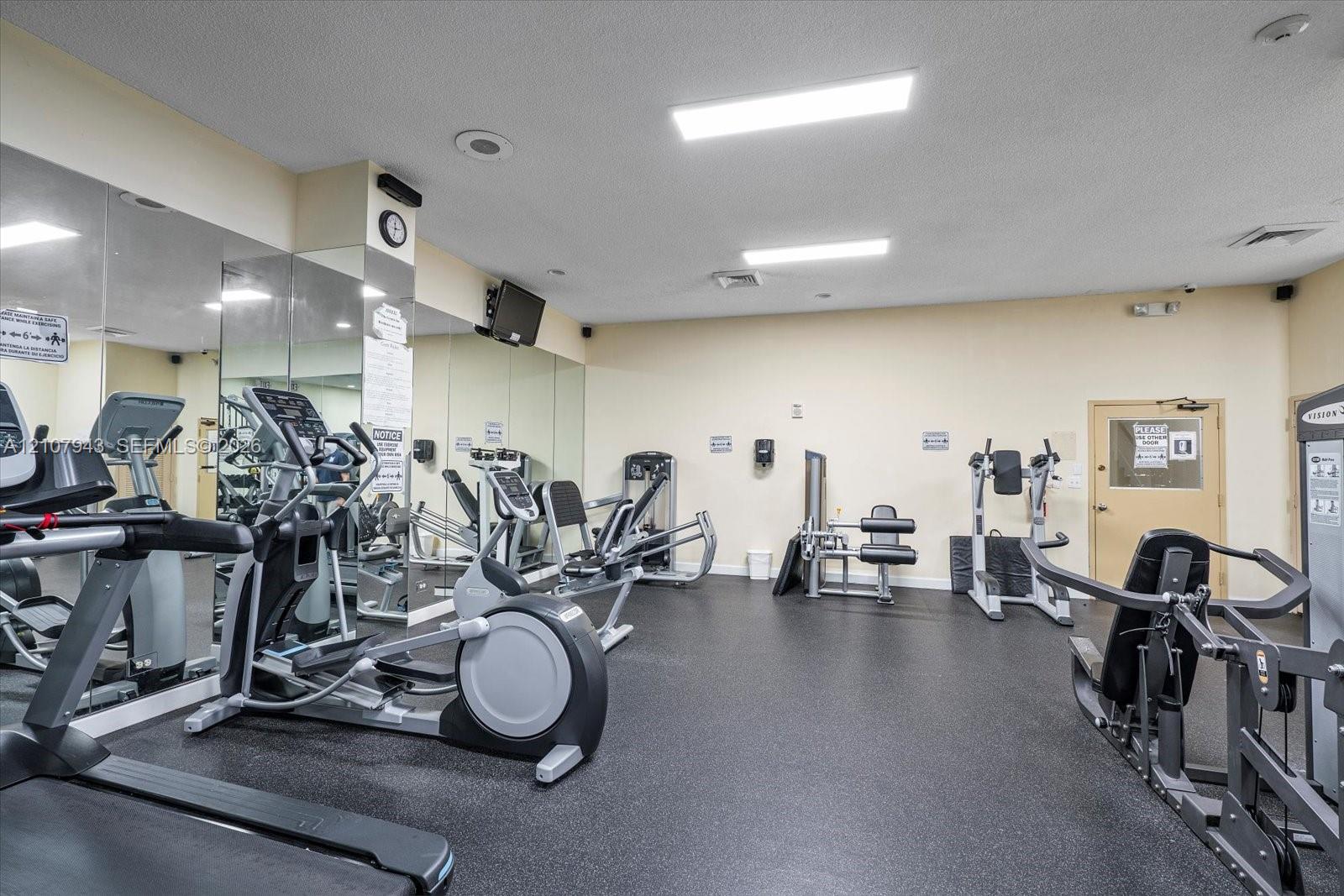 Fitness facility featuring black rubber flooring, wall-to-wall mirrors, recessed lighting, and a solid-core entry door