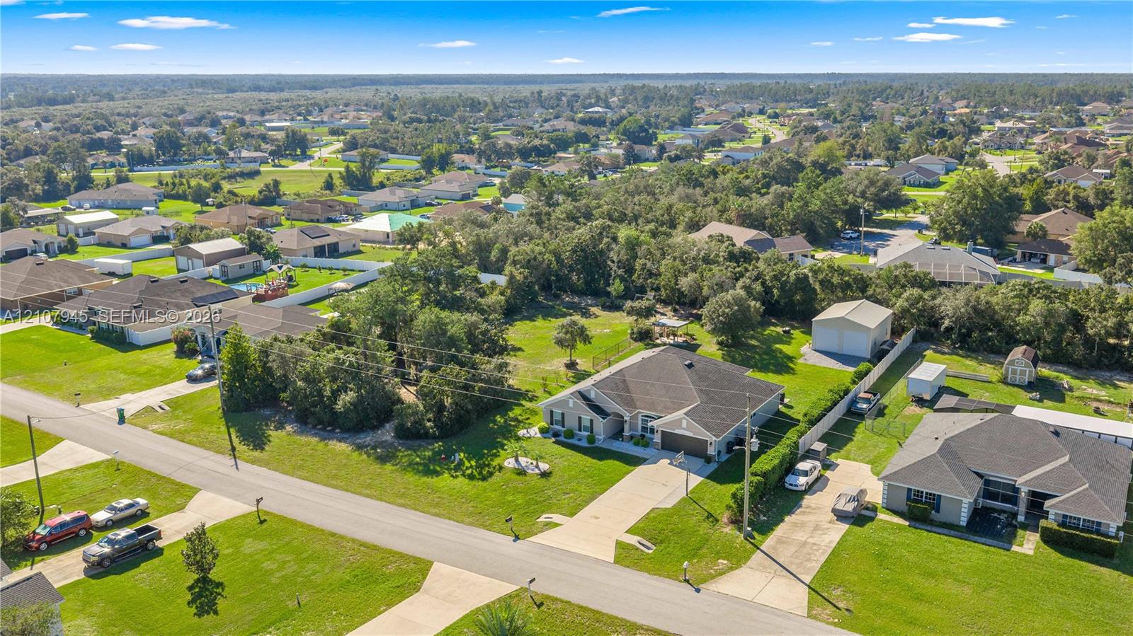 Aerial perspective featuring a single-story residence with a multi-gabled roofline, concrete driveway, attached garage, and detached storage structure on a spacious lot