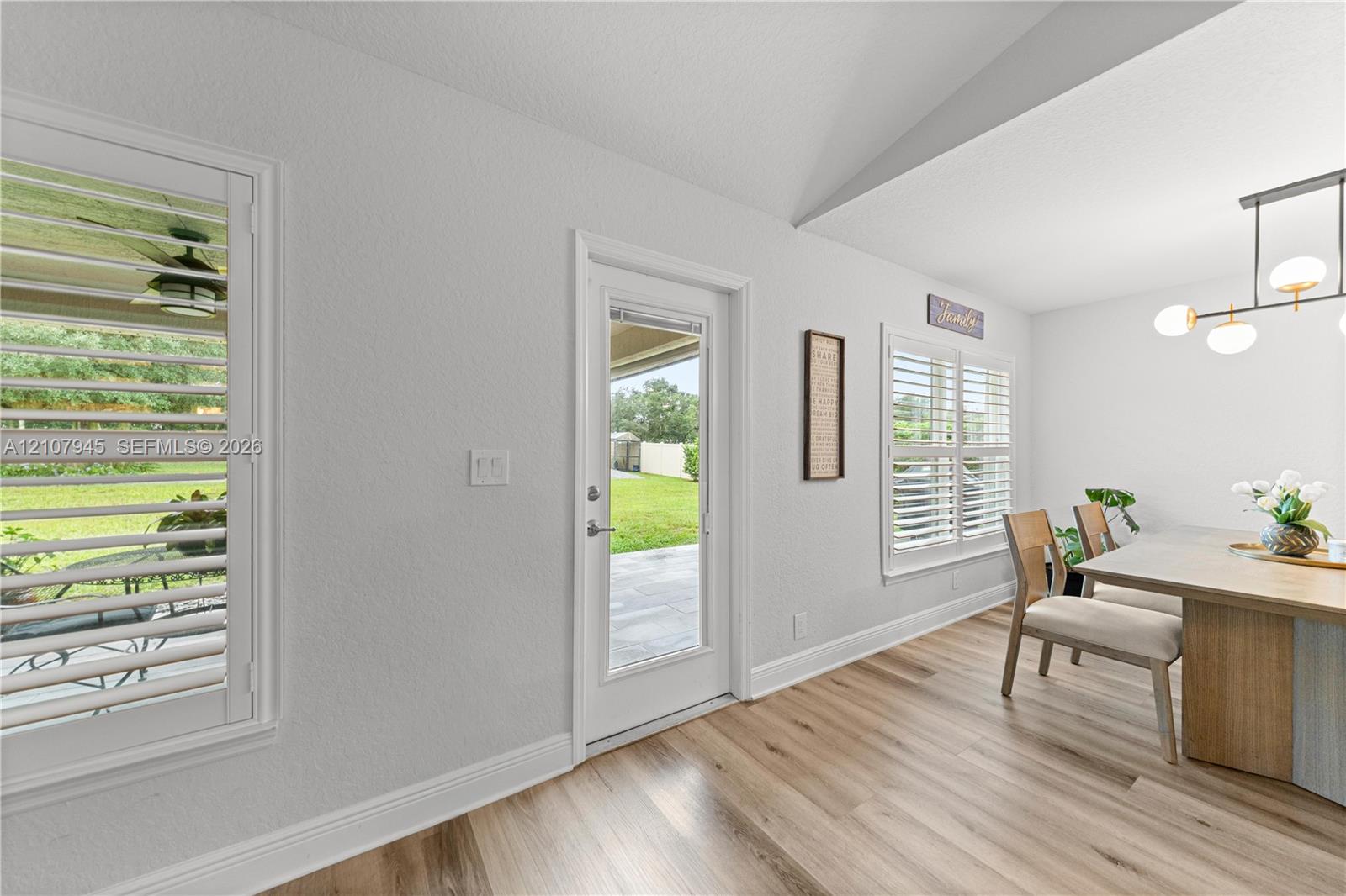 Vaulted ceiling featuring wood-finish flooring, plantation shutters, and a modern linear chandelier