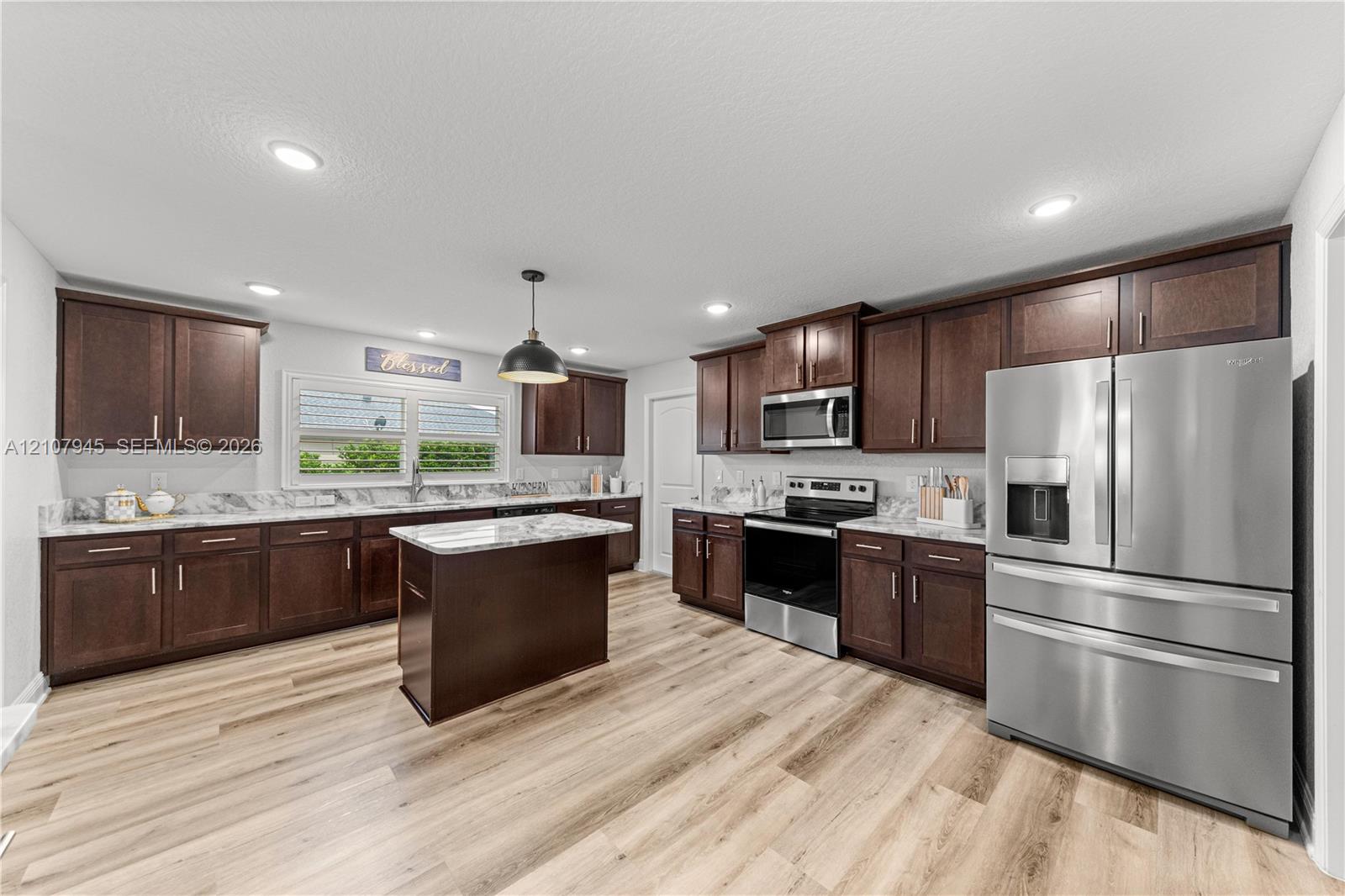 Kitchen featuring dark wood cabinetry, stone-surface countertops, central island, stainless steel appliances, and wood-finish flooring