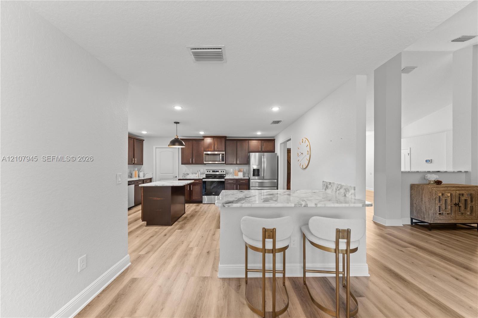 Kitchen featuring dark wood-finish cabinetry, a center island with a stone-finish countertop, stainless steel appliances, and wood-finish flooring