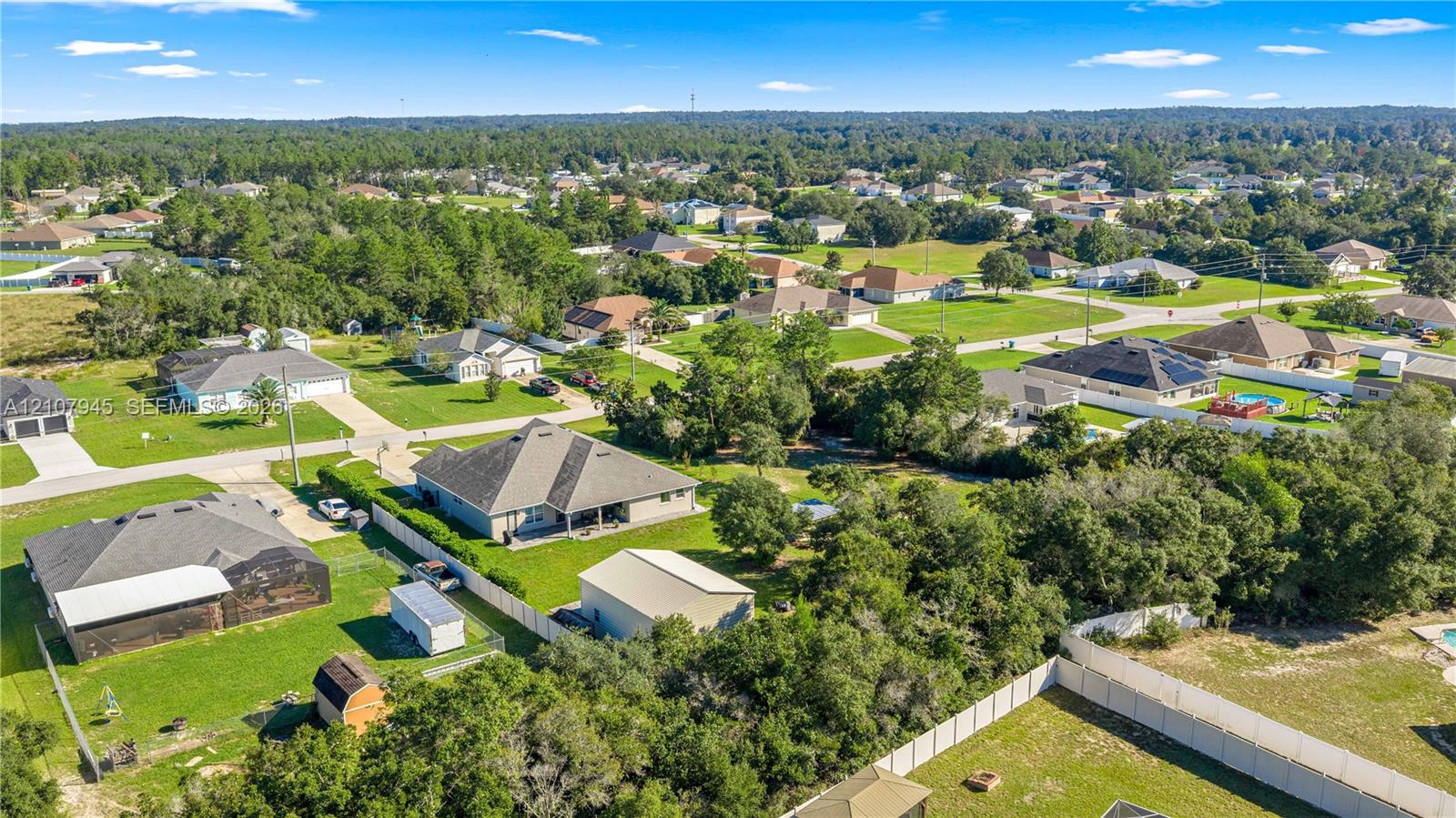 Aerial perspective of the property featuring a detached garage, expansive green space, mature trees, and perimeter fencing