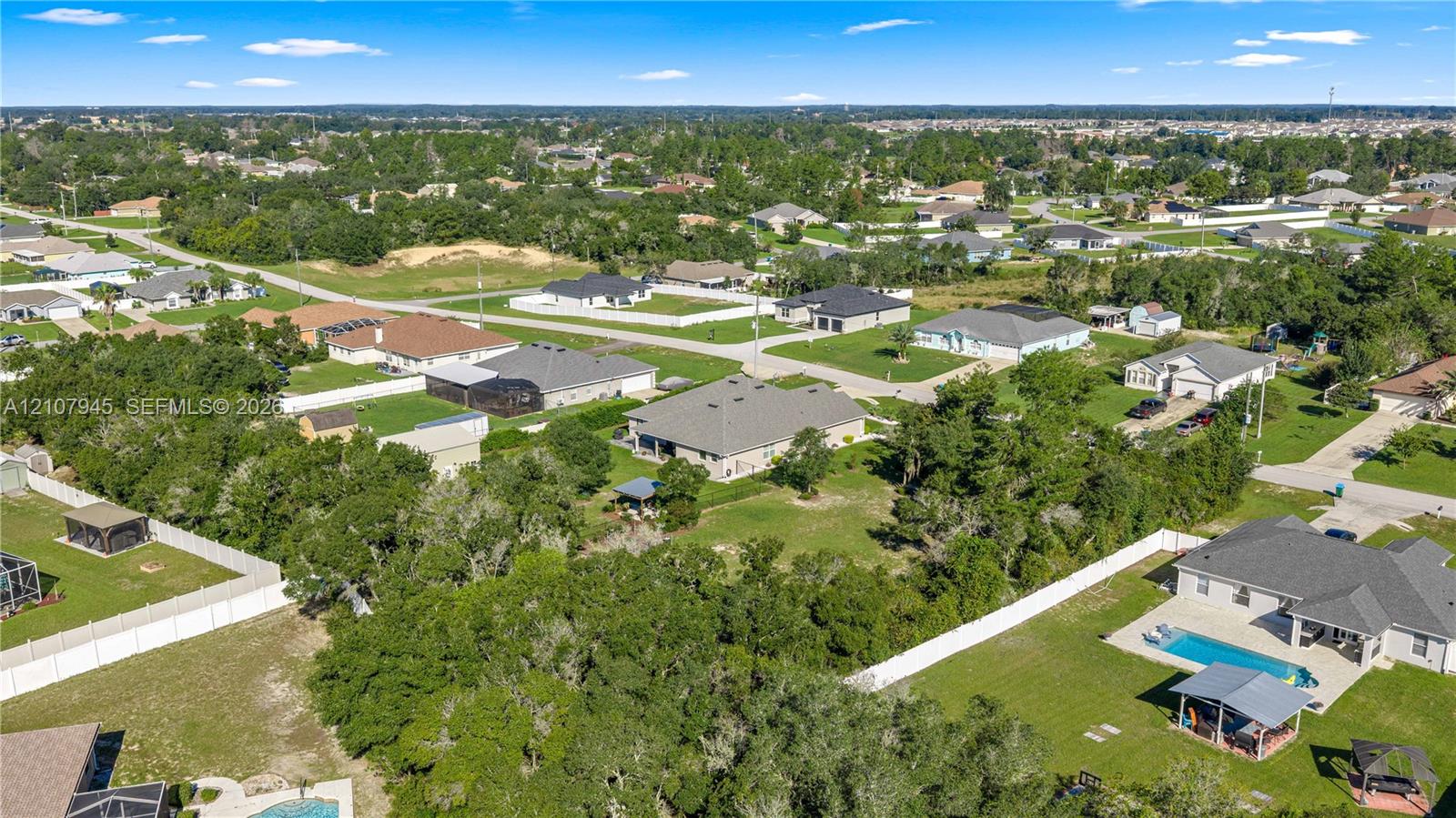 Aerial perspective of a residential lot featuring expansive green space, mature perimeter trees, a private inground swimming pool, and a detached covered pavilion
