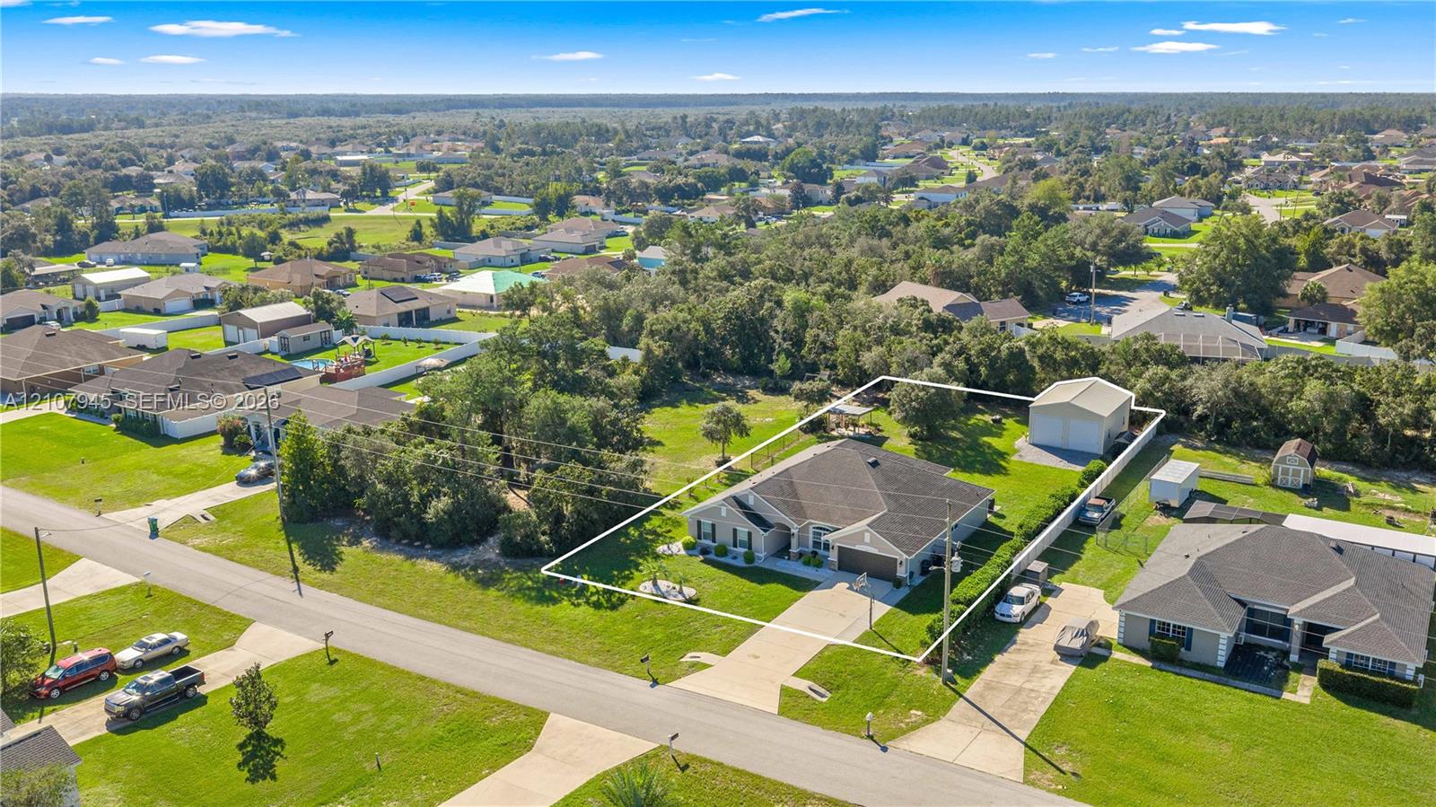 Single-story residence featuring a shingle roof, attached garage, expansive lawn, and detached storage structure