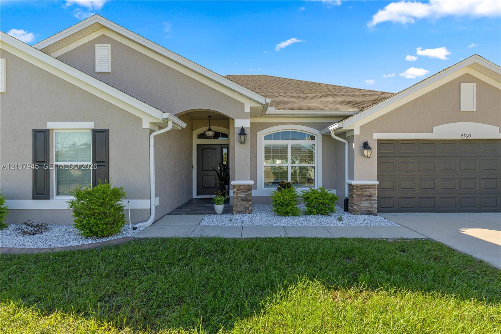 Stucco exterior featuring decorative stone accents, arched entryway, arched front window, multi-gabled roofline, and two-car garage