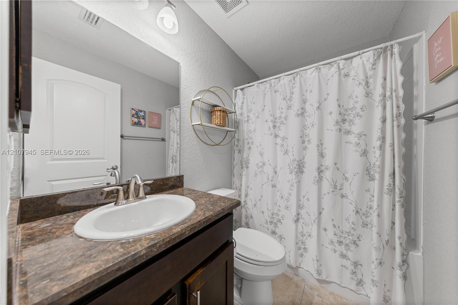 Dark wood vanity with a stone-finish countertop, undermount oval sink, chrome dual-handle faucet, and large wall-mounted mirror