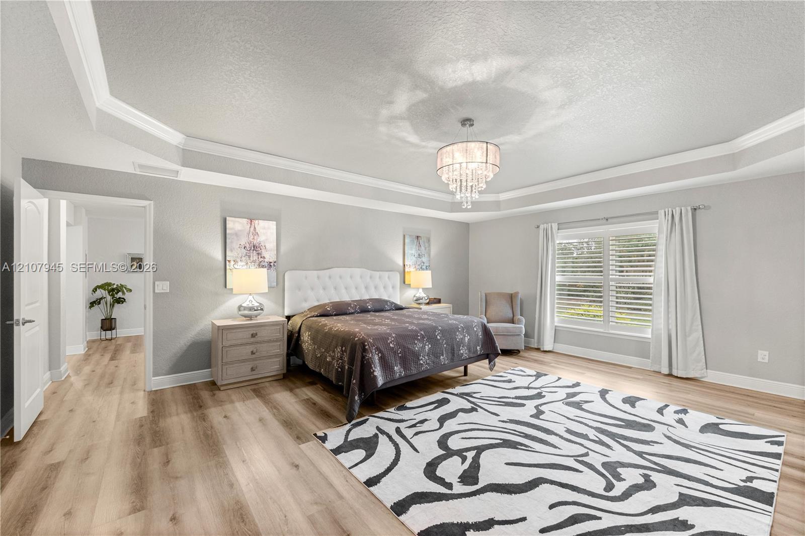 Tray ceiling with crown molding, crystal-style chandelier, wood-finish flooring, and multi-pane windows with horizontal blinds