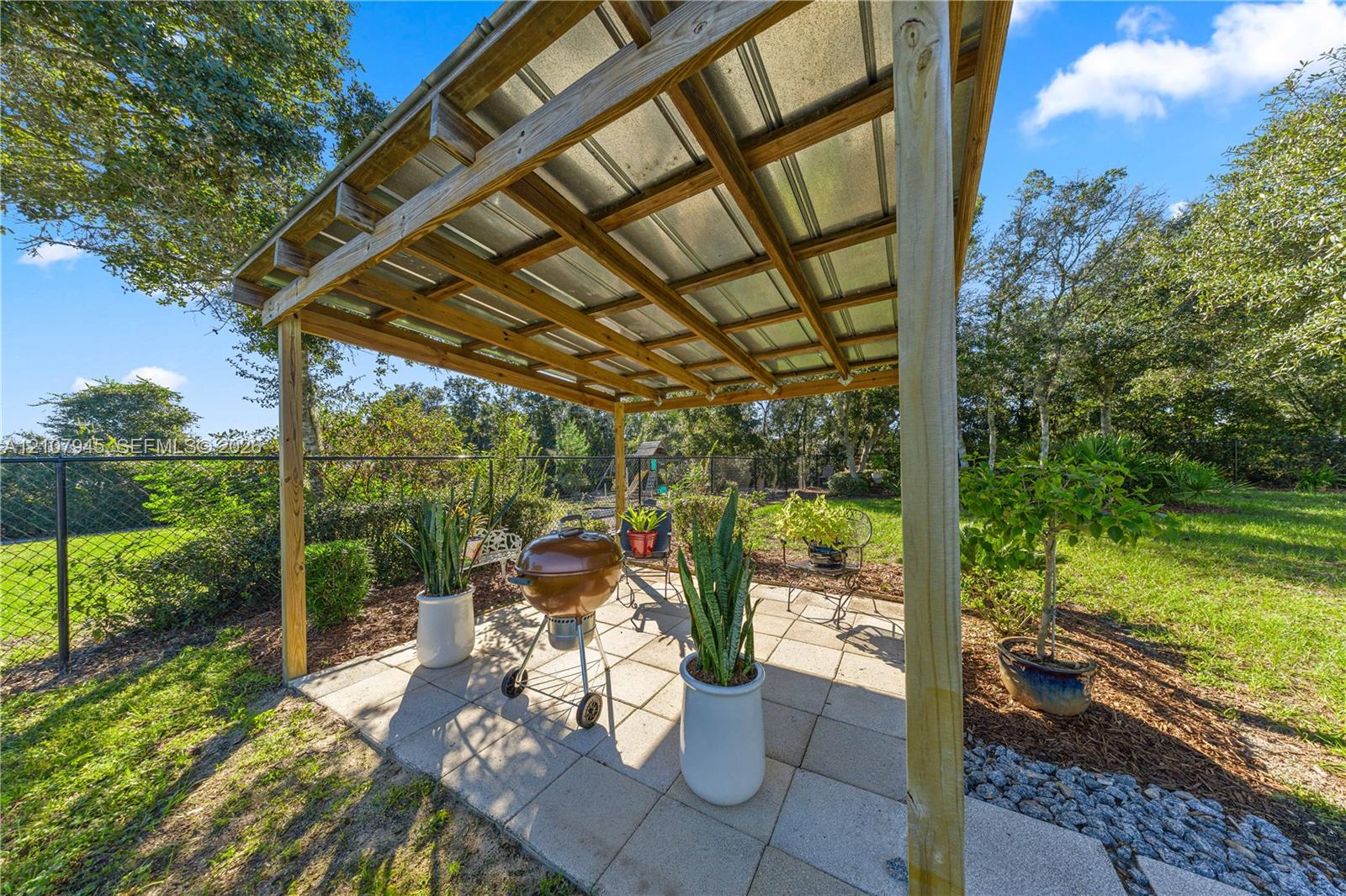 Outdoor pergola with a corrugated metal roof, wood-beam support structure, and concrete paver patio surface
