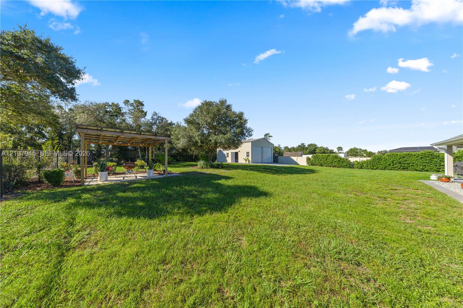 Expansive backyard featuring a large grass lawn, a wood-framed pergola, and a detached two-car garage